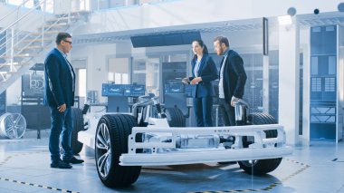 Otomotiv Tasarım Mühendisleri Elektrikli Araç Şasi Prototipi Üzerinde Çalışırken Konuşuyor. Yenilik Laboratuvarı Nda Tesis Konsept Araç Çerçevesi Tekerlekler, Süspansiyon, Motor ve Akü.