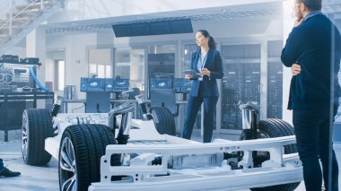 Otomotiv Tasarım Mühendisleri Elektrikli Araç Şasi Prototipi Üzerinde Çalışırken Konuşuyor. Yenilik Laboratuvarı Nda Tesis Konsept Araç Çerçevesi Tekerlekler, Süspansiyon, Motor ve Akü.