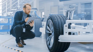 Yüksek Teknoloji Geliştirme Laboratuvarında Tekerlekler, Piller ve Motorlu Elektrikli Araba Şasi Prototipinin Yanında Tablet Bilgisayarda Gözlük ve Sakal İşleri Ile Mühendis.
