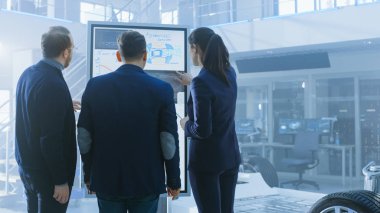 Tasarım Mühendisleri Çeşitli Ekibi Çalışma ve Bir Elektrikli Otomobil Şasi Prototip Yanında İnteraktif Beyaz Tahta bir şey tartışıyor. Araç Çerçeveli Yüksek Teknoloji Laboratuvar Tesisinde.