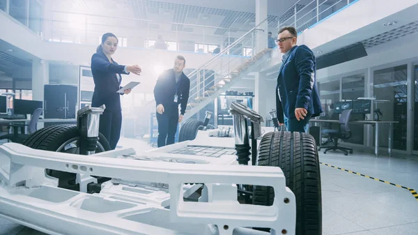 Ingénieurs de conception automobile parler tout en travaillant sur le prototype de châssis de voiture électrique. Dans le concept d'installation de laboratoire d'innovation, le cadre du véhicule comprend les roues, la suspension, le moteur et la batterie . — Photo