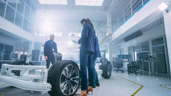 Equipo de Ingenieros de Diseño de Automóviles en las Instalaciones de Innovación Automotriz. Están trabajando en el prototipo del chasis de la plataforma del coche eléctrico que incluye ruedas, suspensión, motor híbrido y batería . — Foto de Stock