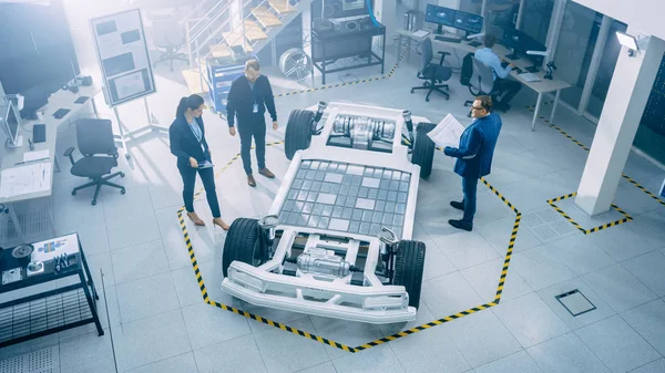 汽车创新设施汽车设计工程师团队。他们正在工作电动车平台底盘原型，包括车轮，悬架，混合动力发动机和电池. — 图库照片