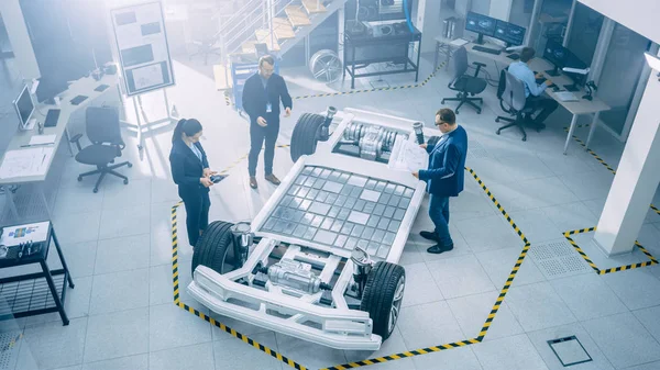 Equipo de Ingenieros de Diseño de Automóviles en las Instalaciones de Innovación Automotriz. Están trabajando en el prototipo del chasis de la plataforma del coche eléctrico que incluye ruedas, suspensión, motor híbrido y batería . — Foto de Stock