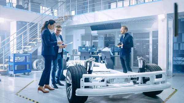 Automotive design ingenjörer pratar medan du arbetar på elbil chassi prototyp. I innovation laboratorie anläggning koncept fordons ram inkluderar hjul, fjädring, motor och batteri. — Stockfoto