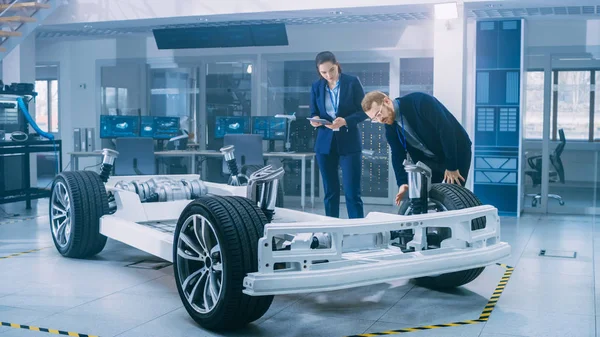 Ingénieurs en conception automobile travaillant sur le prototype de châssis de voiture électrique. Dans le concept d'installation de laboratoire d'innovation, le cadre du véhicule comprend les roues, la suspension, le moteur et la batterie . — Photo