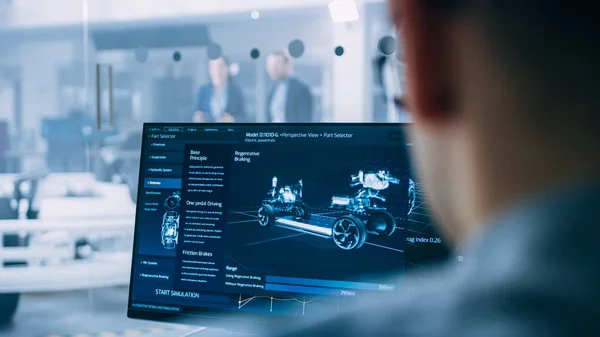 Professional Engineer Works on a Computer with a 3D CAD Software and Tests the Electric Car Chassis Prototype with Wheels, Batteries and Engine Standing in a High Tech Development Laboratory. — Stock Photo, Image