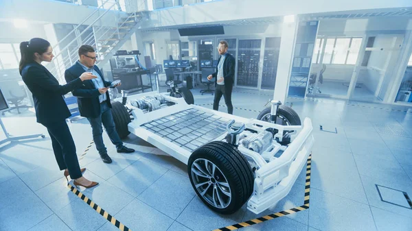 汽车设计工程师向管理委员会代表展示电动汽车底盘原型。概念包括车轮、混合动力发动机和电池. — 图库照片
