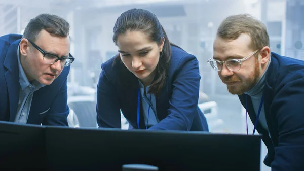 Los ingenieros de diseño automotriz están trabajando y discutiendo algo en una pantalla de computadora junto a un prototipo de chasis de automóvil eléctrico. En las instalaciones de laboratorio de alta tecnología con el marco del vehículo . — Foto de Stock