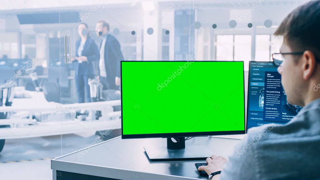 Professional Engineer Works on a Computer with Green Screen Mock-up Template. Electric Car Chassis Prototype with Batteries and Engine Standing in a High Tech Development Laboratory.