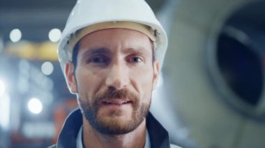 Gülümseyen Profesyonel Ağır Sanayi Mühendisi / İşçi Güvenlik Üniforması ve Sert Şapka Giyen Portresi. Arka planda Odaklanmamış Büyük Endüstriyel Fabrika
