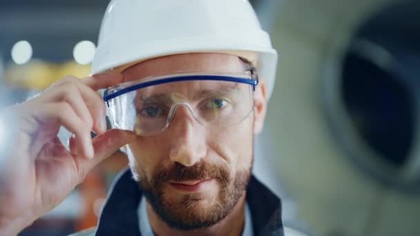 Πορτρέτο του χαμογελαστού επαγγελματία βαριά βιομηχανία μηχανικός / εργαζόμενος φορώντας στολή ασφαλείας, γυαλιά και σκληρό καπέλο. Στο παρασκήνιο Μη εστιασμένο Μεγάλο Βιομηχανικό Εργοστάσιο — Αρχείο Βίντεο
