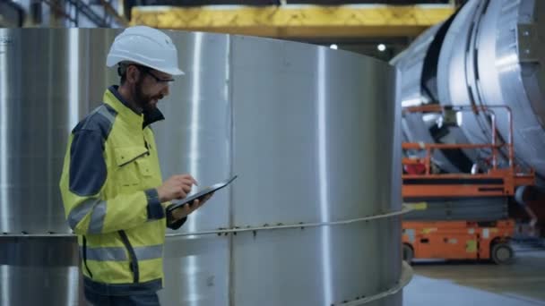 Ingénieur de l'industrie lourde marcher à travers l'usine de fabrication de tuyaux, Utilisez un ordinateur tablette numérique. Installation de construction de pipelines de pétrole, de gaz et de carburant Produits de transport. Vue latérale Mouvement lent 