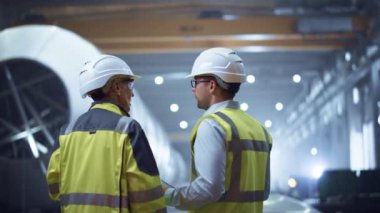 İki Ağır Sanayi Mühendisi Boru İmalat Fabrikası 'nda duruyor, Dijital Tablet Bilgisayar kullanın, Tartışıyorlar. Petrol, Gaz ve Yakıt Taşımacılık Boru Hattı İnşaatı. Geri Görünüm Kıvılcımları Uçuyor