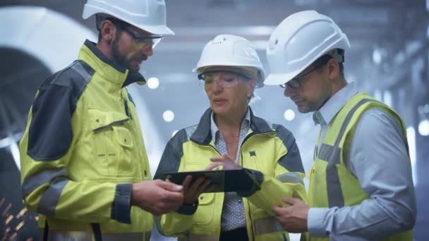 Tres ingenieros de la industria pesada están de pie en la fábrica de fabricación de tuberías, utilice la computadora digital de la tableta, tienen discusión. Tubo grande montado. Diseño y construcción de tuberías de transporte de petróleo, gas y combustibles — Vídeo de stock