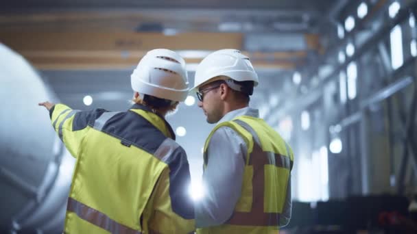 Deux ingénieurs de l'industrie lourde se tiennent dans l'usine de fabrication de tuyaux, utilisent un ordinateur tablette numérique, discutent. Construction d'un pipeline de transport de pétrole, de gaz et de combustibles. Vue arrière Sparks Flying