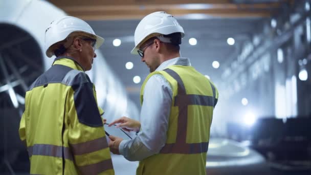 Deux ingénieurs de l'industrie lourde se tiennent dans l'usine de fabrication de tuyaux, utilisent un ordinateur tablette numérique, discutent. Construction d'un pipeline de transport de pétrole, de gaz et de combustibles. Vue arrière Sparks Flying