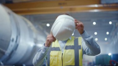 Genç Profesyonel Ağır Sanayi Mühendisi Portresi / İşçi Giyen Güvenlik Yeleği, Hardhat koyarak. Arka Planda Odaksız Büyük Sanayi Fabrikası nerede Kaynak Sparks Uçan. Yavaş Çekim