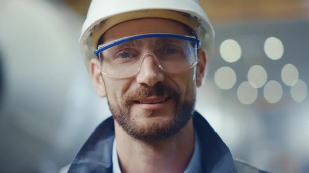 Portré a profi nehézipari mérnök / munkás viselő biztonsági egyenruha, szemüveg és keménykalap mosolygás. A háttérben fókuszálatlan nagy ipari gyár, ahol hegesztő szikrák repülő — Stock videók