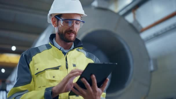 Portrait of Professional Heavy Industry Engineer / Worker Wearing Safety Uniform and Hard Hat Uses Tablet Computer. In the Background Construction Factory for Oil, Gas and Fuels Transport Pipeline — Stock Video