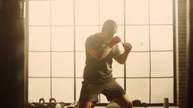 Güçlü ve Yakışıklı Erkek Boxer Büyük Pencere ile Bir Loft Spor Salonu'nda Dışarı Çalışıyor. Erkeksi Atlet Havada Punches pratik olduğunu. Ciddi ve enerjik. Sıcak Işıkla Aydınlatılmış Oda