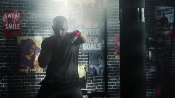 Silný a pohledný mužský boxer pracuje v podkrovní tělocvičně s motivačními plakáty na zdech. Mužský atlet se cvičí ve vzduchu. Je vážný a energický. Místnost je tmavá. — Stock video