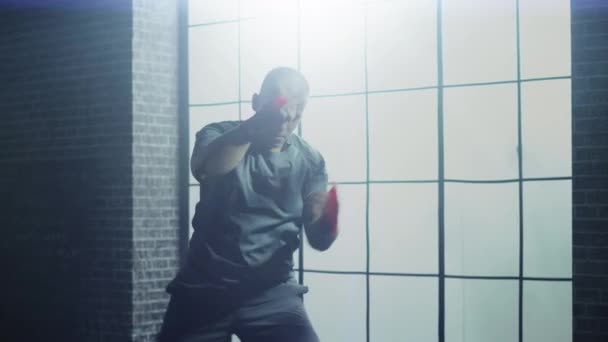 Boxeador masculino fuerte y guapo está trabajando en un gimnasio loft con carteles motivacionales en las paredes. El atleta masculino está practicando golpes en el aire. Es serio y enérgico. Ventana grande detrás de él . — Vídeo de stock