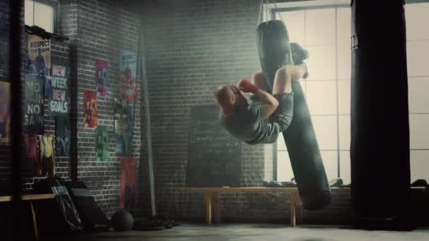 Punching Bag Crunches. Hombre Masculino Fuerte Abrazando la Bolsa con Sus Piernas y Bombeando Sus Abdominales y Músculos Centrales. Trenes masculinos guapos en un gimnasio y caídas al final. Accidente deportivo que causa dolor de espalda . — Vídeo de stock