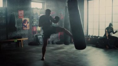 Güçlü ve Yakışıklı Erkek Kickboxer Duvarlarda Motivasyonposterler ile bir Loft Spor Salonu'nda Dışarı Çalışıyor. Erkeksi Atlet Bir Boks Çantası Punches pratik olduğunu. Ciddi ve Enerjik.