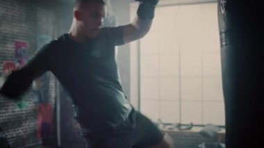 Güçlü ve Yakışıklı Erkek Kickboxer Duvarlarda Motivasyonposterler ile bir Loft Spor Salonu'nda Dışarı Çalışıyor. Erkeksi Atlet Bir Boks Çantası Punches pratik olduğunu. Ciddi ve Enerjik.