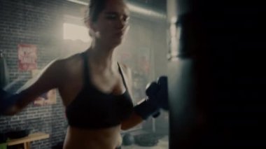 Fit Atletik Kadın Kickboxer Punches ve Hits Punching Çanta Motivasyonel Posterler ile bir Loft Spor Salonunda bir egzersiz sırasında. Yoğun Kendini Savunma Eğitiminden Sonra Yorgun ve Yorgun.