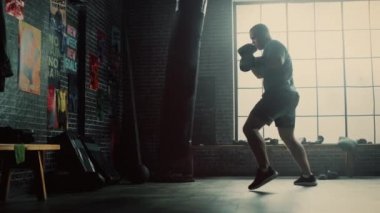 Güçlü ve Yakışıklı Erkek Kickboxer Duvarlarda Motivasyonposterler ile bir Loft Spor Salonu'nda Dışarı Çalışıyor. Erkeksi Atlet Bir Boks Çantası Punches pratik olduğunu. Ciddi ve Enerjik.