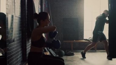 Güzel Fit Esmer Kickboxer Atlet Motivasyonposterler ile Loft Gym bir Bankta Oturan. Mavi Dövüş Eldivenlerini Takıyor. Kadın Ayağa Kalkar ve Onun Yoğun Boks Eğitimi Devam Ediyor.