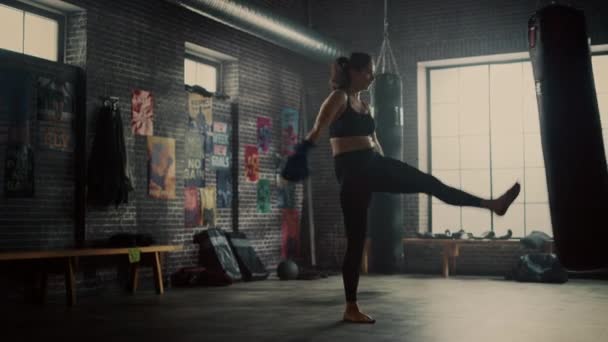 Fit Athletic Woman Kickboxer golpea el saco de boxeo con su pierna por última vez durante un entrenamiento en un gimnasio loft con carteles motivacionales. Ella está agotada y cansada después de su entrenamiento de autodefensa . — Vídeos de Stock