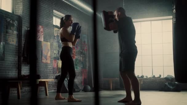 Fit Athletic Woman Kickboxer socos as almofadas de perfuração durante um treino no ginásio. Ela é bonita e energética. Forte instrutor está segurando as almofadas de boxe. Treinamento Intenso de Autodefesa . — Vídeo de Stock