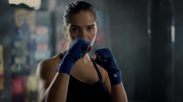 Portret pięknej Fit brunetka Kickboxer stwarzające przed kamerą z rękami owinięte w niebieskie Handwrapping. Jej brązowe oczy odzwierciedlają zaufanie i determinację. Ona jest w podziemnej siłowni. — Wideo stockowe