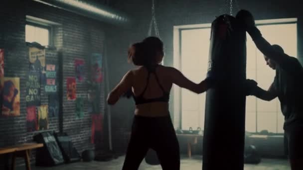 Fit atletische vrouw kickboxer stoten en hits de Pons tas tijdens een training in een loft Gym. Ze is mooi en energiek. Sterke trainer houdt de BoKS zak. Intense zelfverdediging training. — Stockvideo