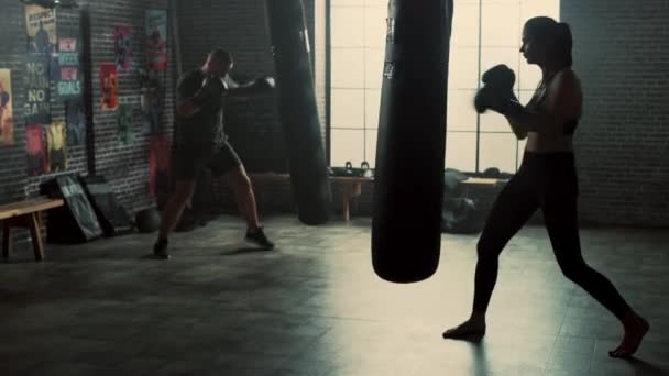 Dwóch młodych Kickboxers praktyka w siłowni Loft. Silny męski człowiek i Athletic piękna kobieta praktyka stemple na worek bokserski. Są one aktywne i energiczny z ich treningu. — Wideo stockowe