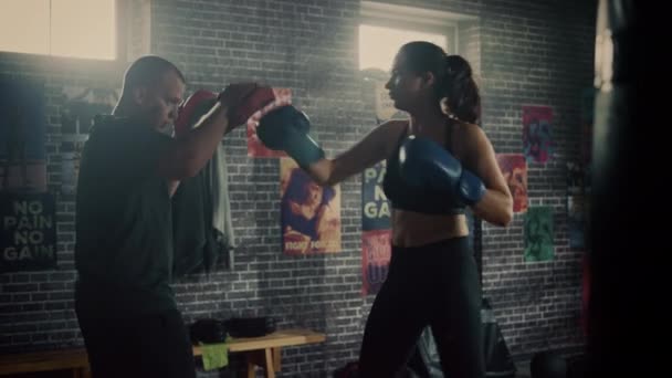 Fit Athletic Woman Kickboxer socos e bate as almofadas de perfuração durante um treino em um ginásio Loft. Ela é bonita e energética. O Treinador Forte está a segurar os Boxing Pads. Treinamento Intenso de Autodefesa . — Vídeo de Stock