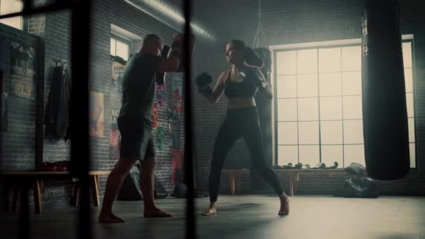Fit atletická žena kickboxer propíchne děrovací destičky během cvičení v tělocvičně. Je krásná a energická. Silný trenér drží boxovací polštářky. Intenzivní výcvik sebeobrany. — Stock video