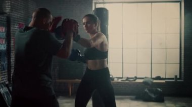 Fit Atletik Kadın Kickboxer Punches ve Bir Loft Spor Salonu'nda bir egzersiz sırasında Punching Pedleri Hits. Çok güzel ve enerjik. Güçlü Koç Boks Pedleri tutuyor. Yoğun Kendini Savunma Eğitimi.