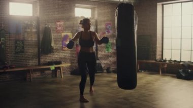 Fit Atletik Kadın Kickboxer Punches ve Hits Punching Çanta Motivasyonel Posterler ile bir Loft Spor Salonunda bir egzersiz sırasında. Yoğun kendini savunma eğitiminden sonra bitkin ve yorgun. Sıcak Işık.