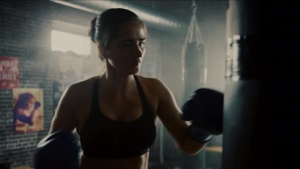 Fit Athletic Woman Kickboxer golpea y golpea el saco de boxeo durante un entrenamiento en un gimnasio loft con carteles motivacionales. Ella está agotada y cansada después de su intenso entrenamiento de autodefensa . — Vídeo de stock