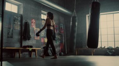 Güzel Fit Esmer Kickboxer Atlet Motivasyonposterler ile Loft Gym bir Tezgah üzerinde Oturur. Nefesini Tutuyor ve Dövüş Eldivenlerini Çıkarıyor. Yoğun Eğitimden Sonra Yorgun.