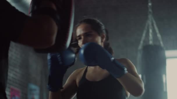 Fit Athletic Woman Kickboxer golpea las almohadillas de perforación durante un entrenamiento en el gimnasio. Es hermosa y enérgica. El entrenador fuerte sostiene las almohadillas de boxeo. Intenso Entrenamiento de Autodefensa. Disparo de cámara lenta . — Vídeo de stock