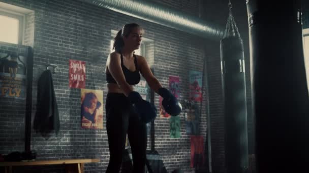 Mooie pasvorm brunette kickboxer staande in Loft Gym met motiverende posters. Ze vangt haar adem en zet haar intense zelfverdediging voort. Atleet heeft zweet op haar gezicht en lichaam. — Stockvideo