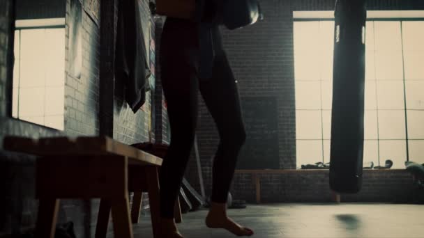 Bella forma bruna Kickboxer atleta si siede su una panchina in palestra Loft con poster motivazionali. Sta respirando e togliendo i guanti da combattimento. E 'stanca dopo un allenamento intenso. . — Video Stock