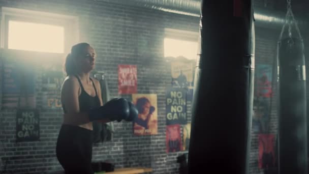 Fit Athletic Woman Kickboxer socos e bate o saco de perfuração durante um treino em um ginásio Loft com cartazes motivacionais. Ela está exausta e cansada após seu intenso treinamento de autodefesa . — Vídeo de Stock