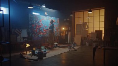 Yetenekli Kadın Sanatçı Bir Tabloya Yürüyor ve Modern Soyut Yağlı Boyama Boyası Üzerinde Çalışmaya Başlıyor. Karanlık Yaratıcı Stüdyoda Büyük Resim Easel Aydınlandı, Araçlar Her Yerde