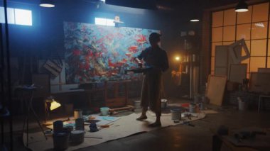 Yetenekli Kadın Sanatçı Modern Soyut Yağ Boyama, Sıçratma ve Damlatma Kullanımı ve Fırça Teknikleri üzerine çalışıyor. Dark Credio Studio Large Picture Stands on Easel Aydınlanmış. Yavaş Hareket